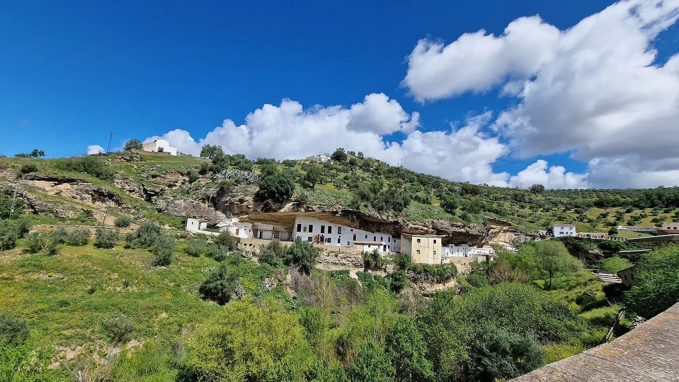 White houses built under a long rock overhang on a green hillside at Setenil de las Bodegas