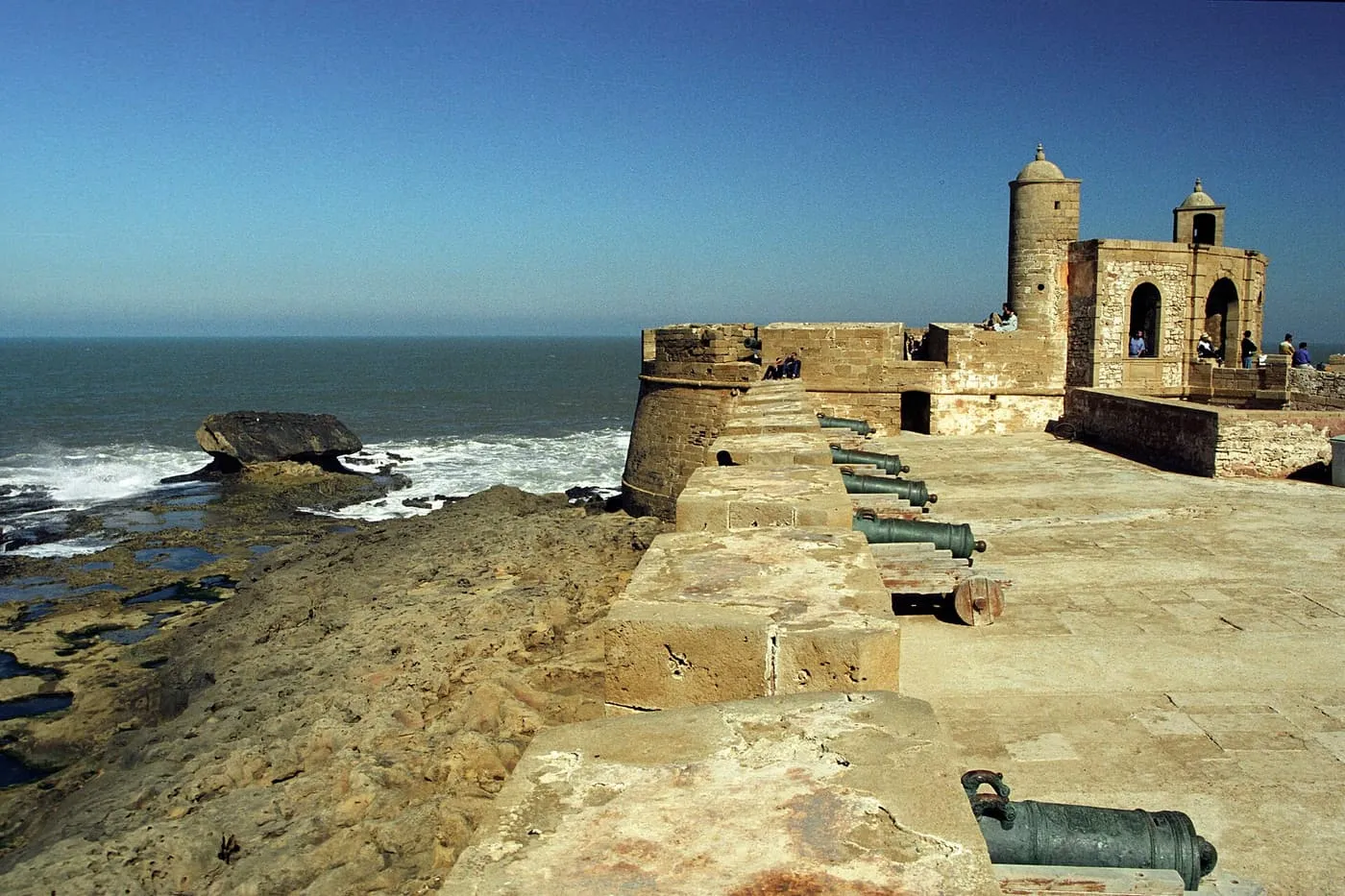 Bronze cannons along the seafront rampart of Essaouira's Skala, with the Atlantic to the left and a round tower ahead