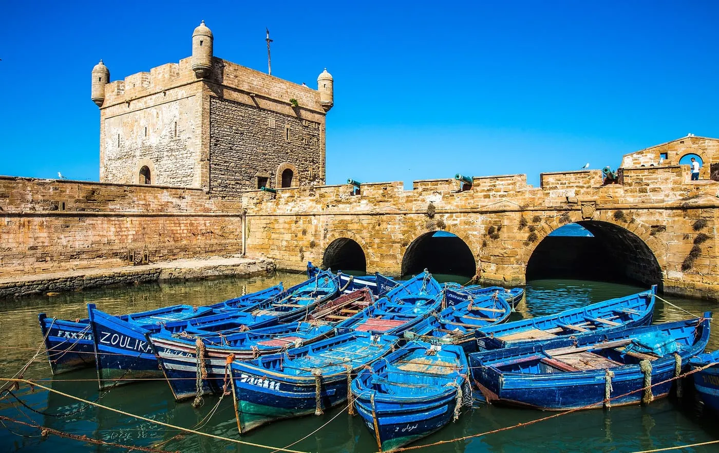 Blue fishing boats moored below the Skala du Port tower and its arched sea wall