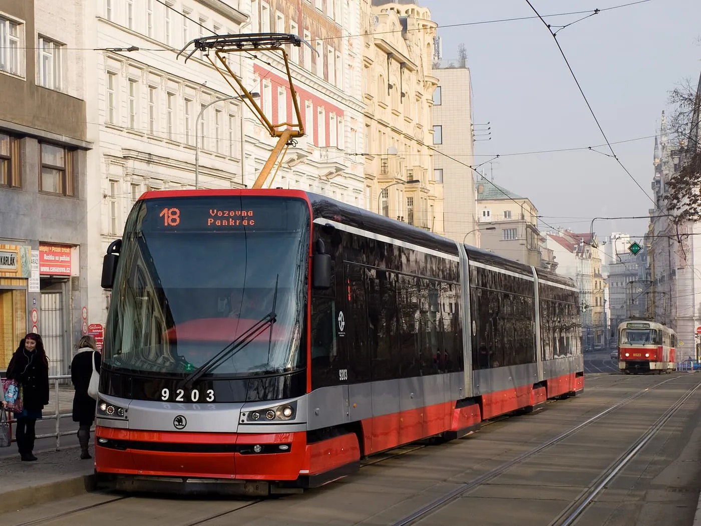 A modern red and grey Škoda 15T tram on line 18 in a Prague street