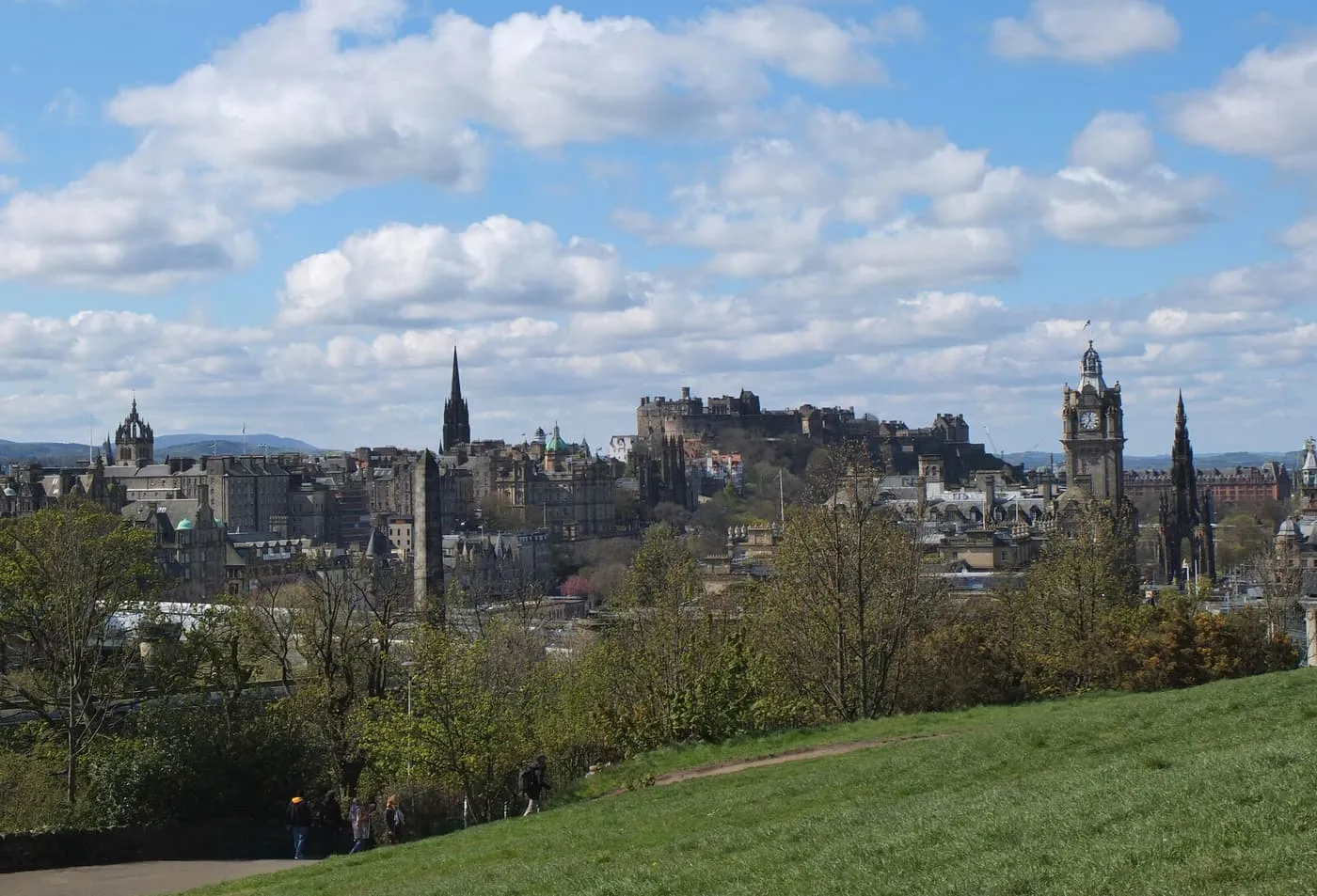 Edinburgh's skyline from Calton Hill: the castle, the Balmoral clock tower and the Scott Monument above the trees, under a sky of broken cloud