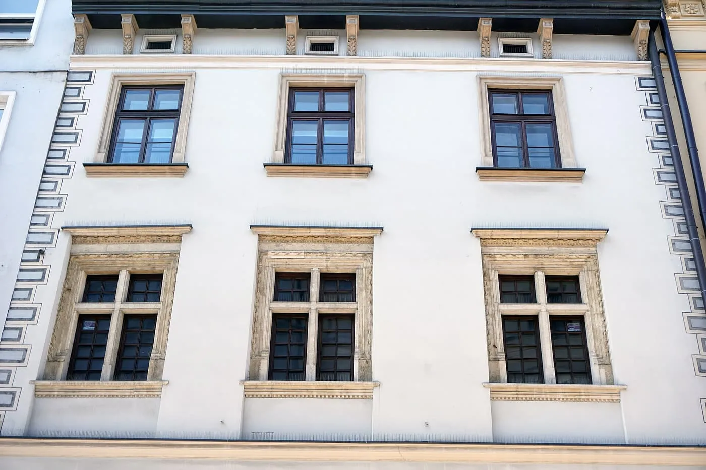 The upper floors of a white townhouse with stone-framed windows under a cornice