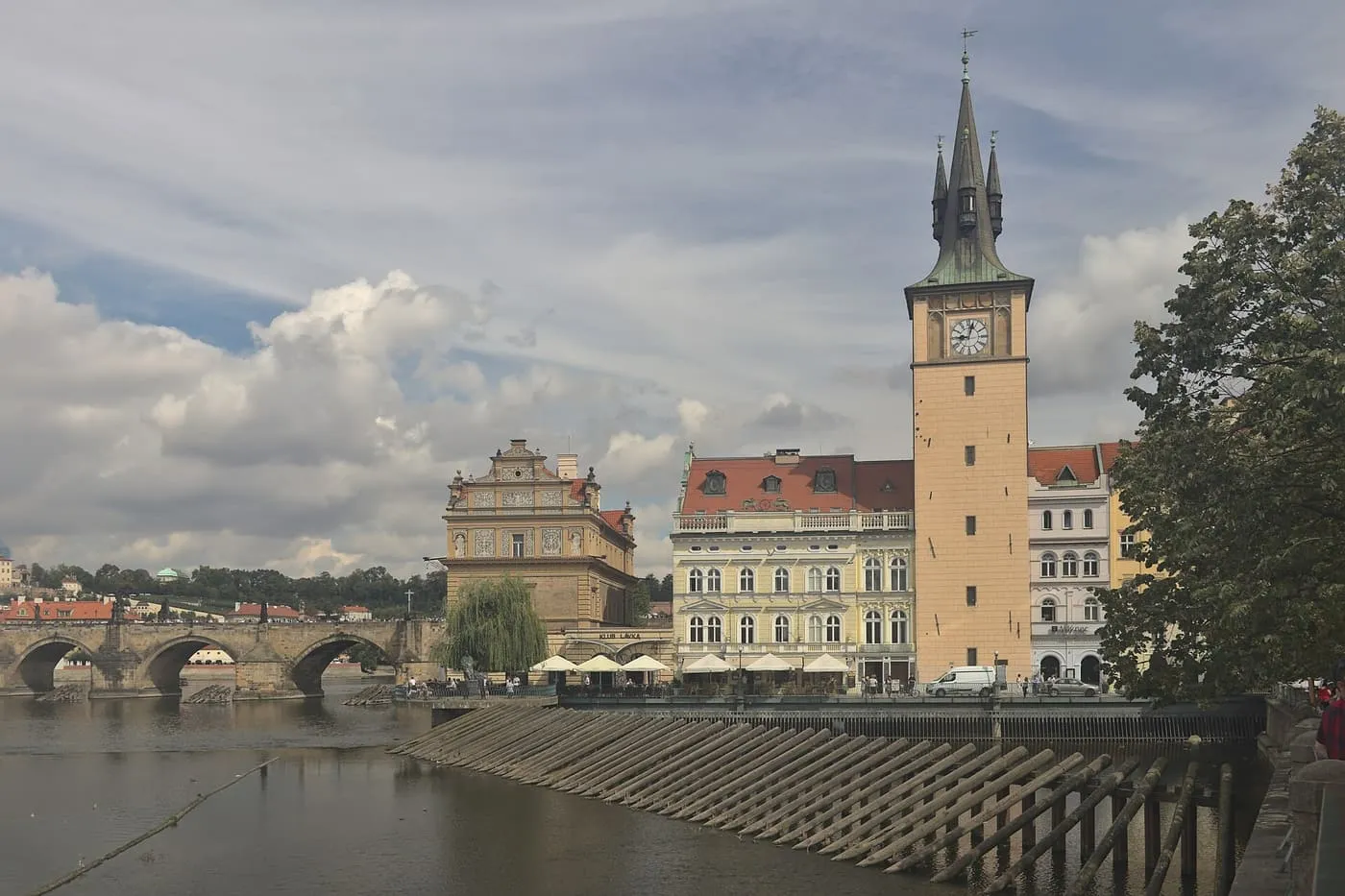 The Smetana Museum, a neo-Renaissance building with a gabled front, beside a tall clock tower on the Vltava embankment, with Charles Bridge on the left
