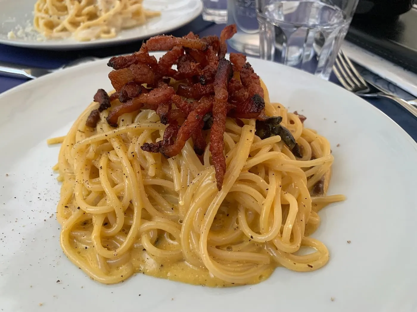 A plate of spaghetti carbonara topped with crisp strips of cured pork and black pepper