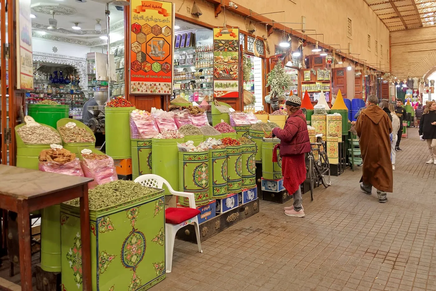 A covered spice market in Marrakech, with painted green bins of spices, herbs and dried goods along a tiled passage