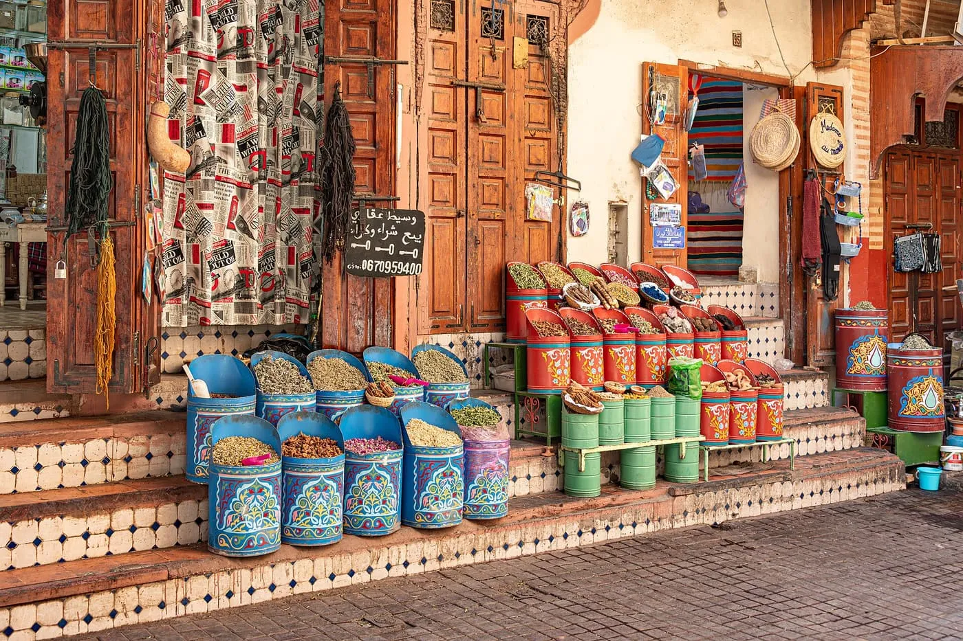 Blue and green tin tubs of spices and herbs on tiled steps outside a shop with carved wooden doors