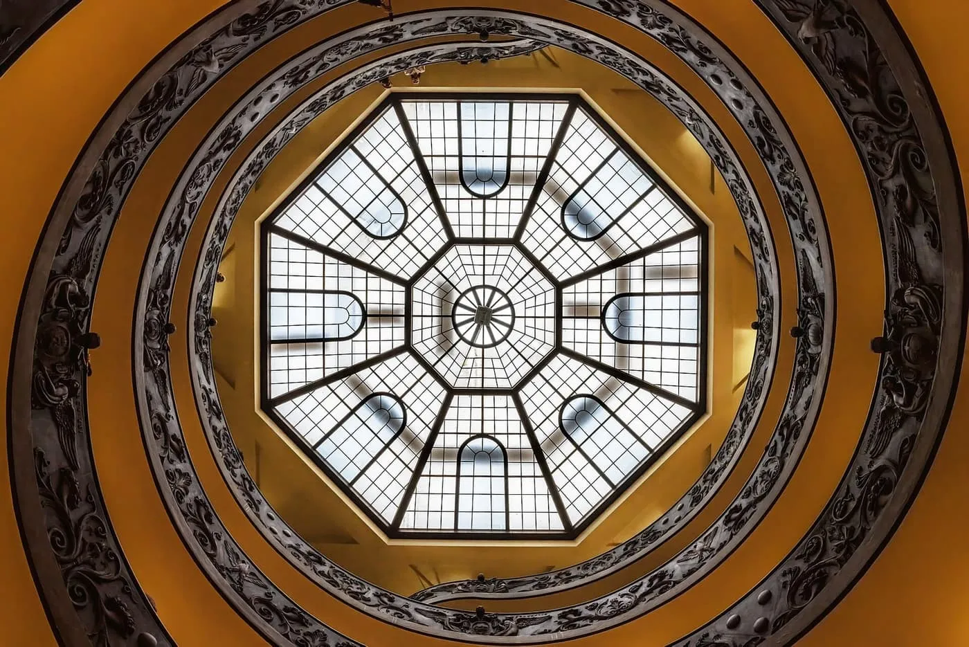 Looking up a spiral staircase in the Vatican Museums to an octagonal glass skylight