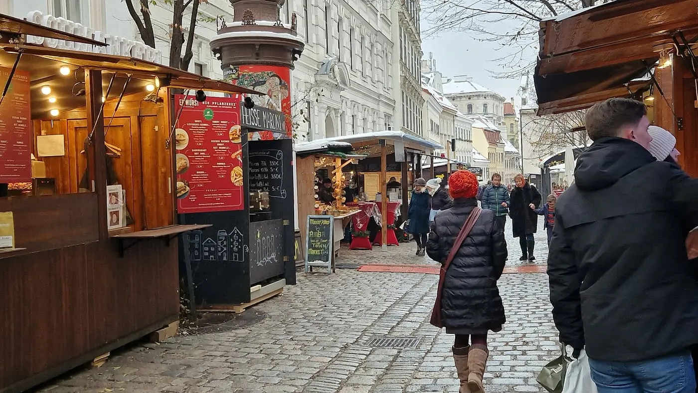 A cobbled Spittelberg lane lined with wooden market huts, with pale Biedermeier house fronts beyond