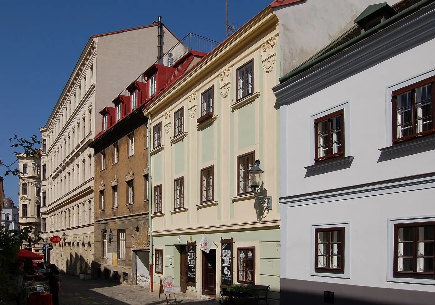 Pastel-fronted Biedermeier houses along a narrow Spittelberggasse in Neubau, under a clear blue sky