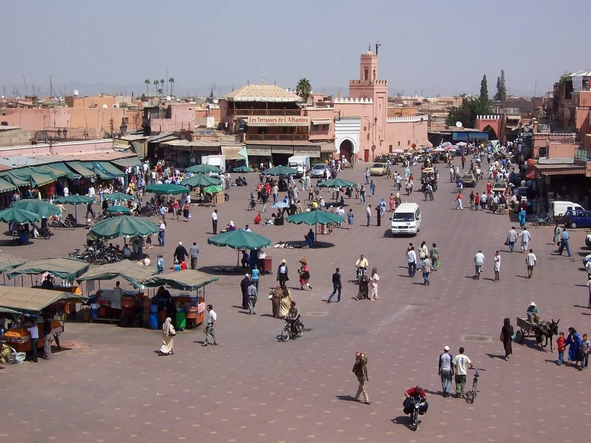 Jemaa el-Fnaa by day from a high vantage, with green market umbrellas and a few people crossing the paved square