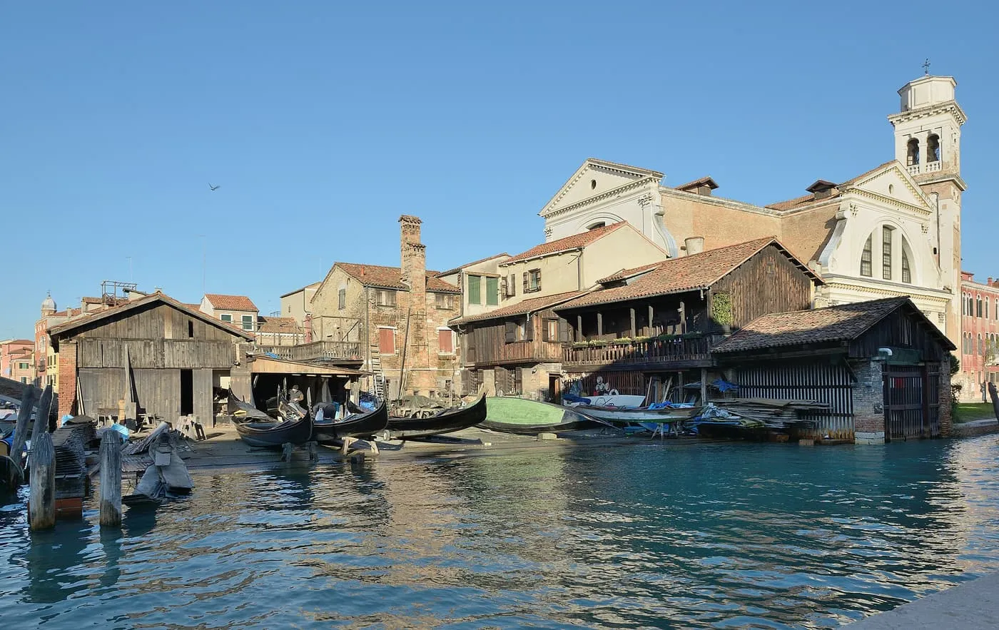The wooden sheds of the Squero di San Trovaso with gondolas drawn up on the bank and the church of San Trovaso behind