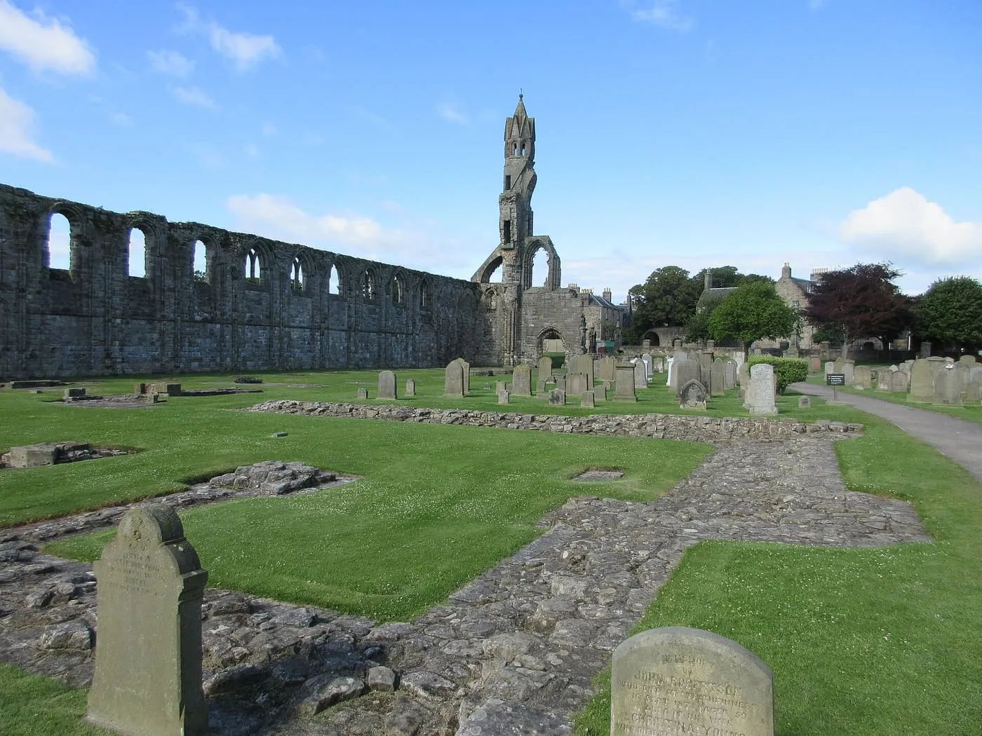 The long ruined nave wall and tower of St Andrews Cathedral above a lawn of old gravestones