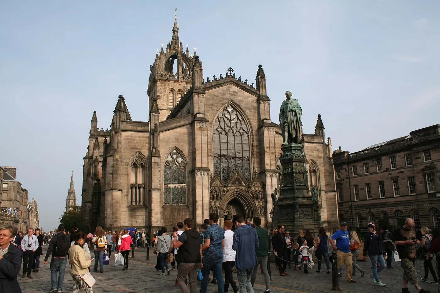 The west front of St Giles' Cathedral with its crown spire and a bronze statue on a tall plinth, with people crossing the cobbles in front