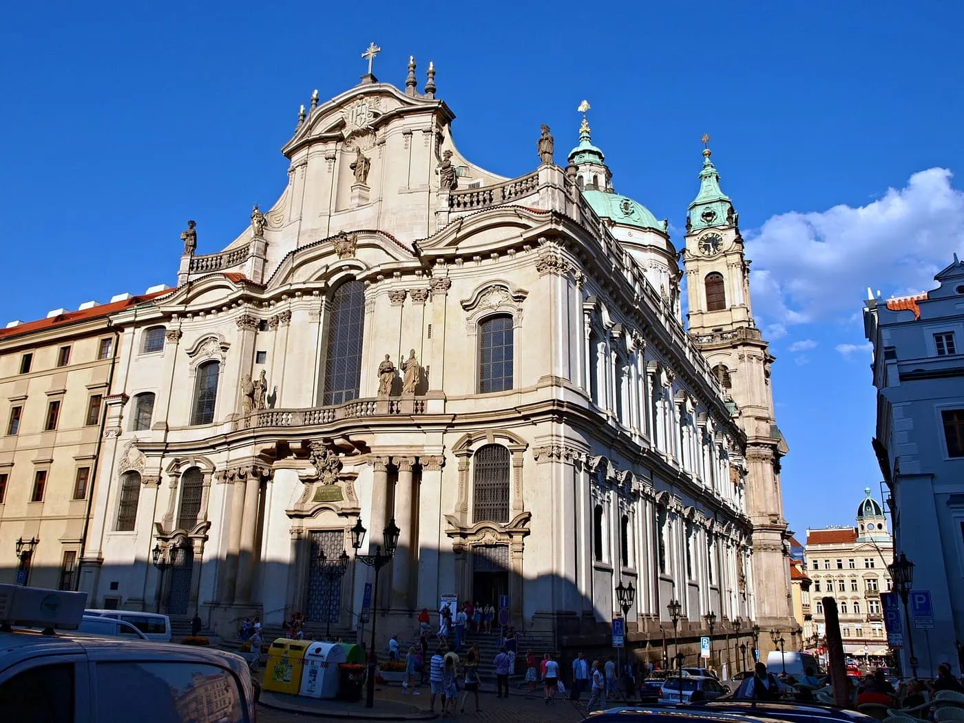 The curved Baroque facade of St Nicholas Church on Lesser Town Square, with its green dome and belfry behind