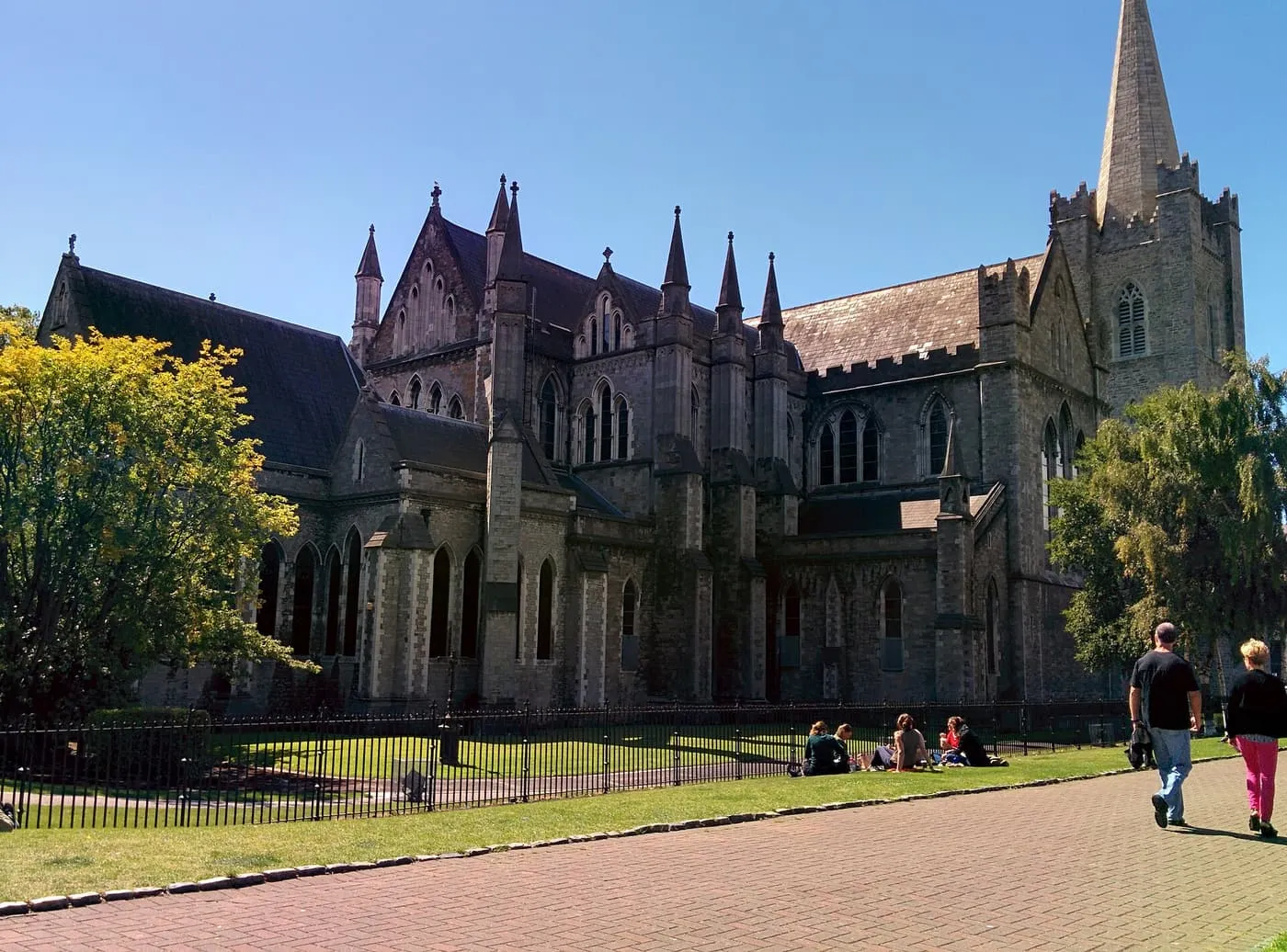 The grey stone east end and spire of St Patrick's Cathedral behind a railing, seen across lawns in St Patrick's Park
