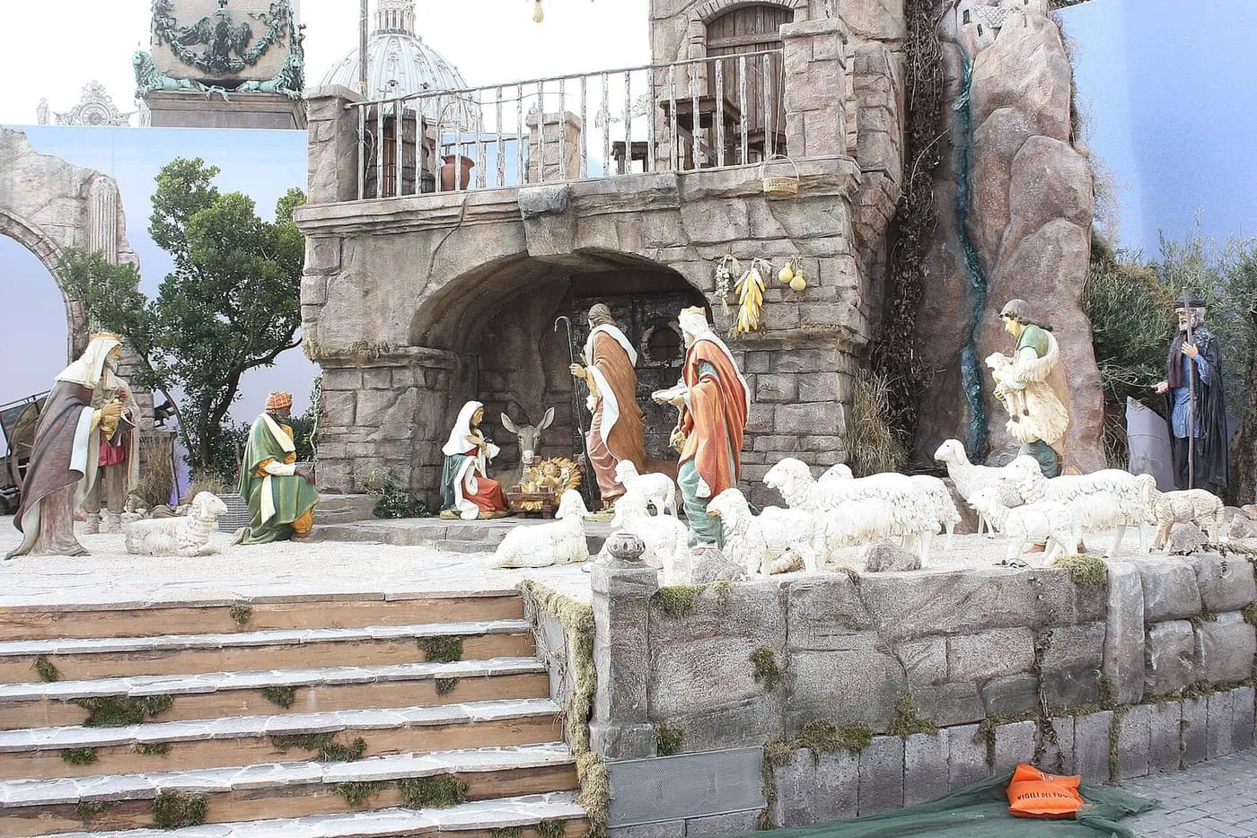 Life-size nativity figures on a stone stage in St Peter's Square, with sheep in the foreground