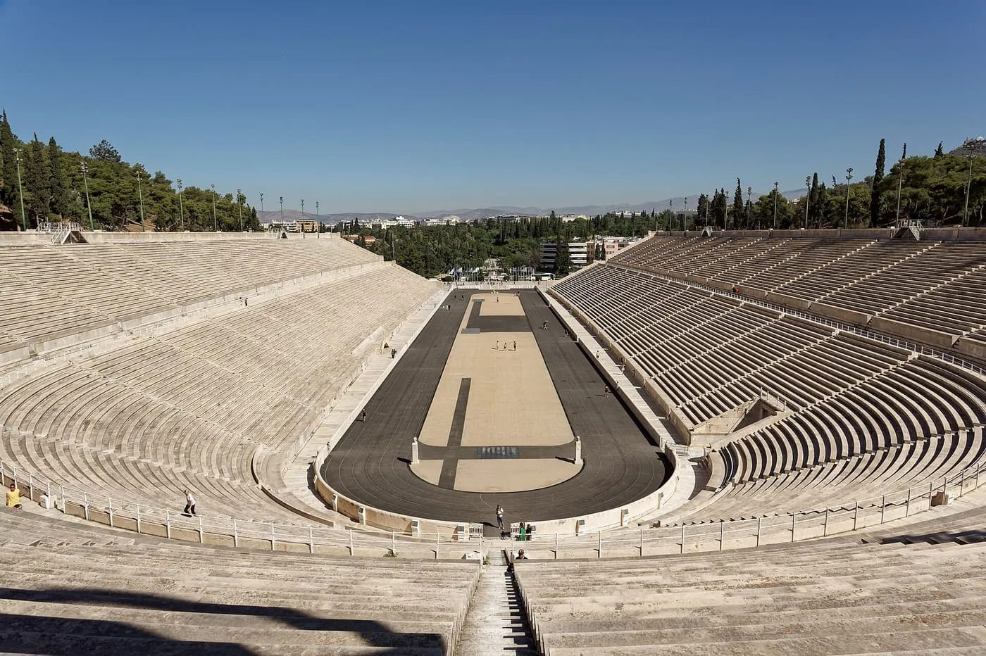 The horseshoe of white marble seating of the Panathenaic Stadium around its running track, seen from the top tier on a clear day