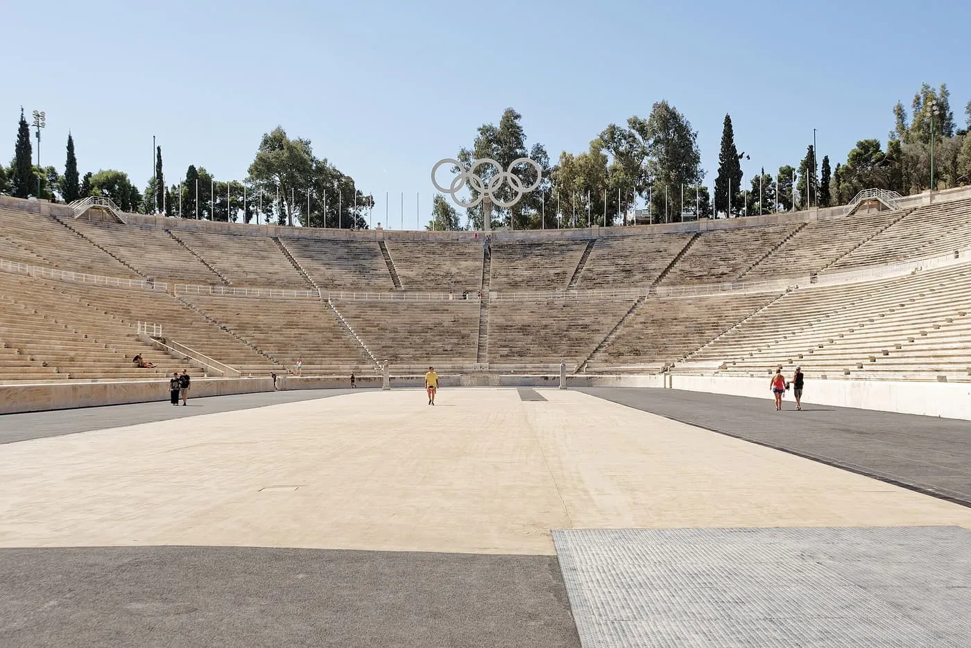 The sand-coloured running track of the Panathenaic Stadium with the curved marble seating and the Olympic rings behind it
