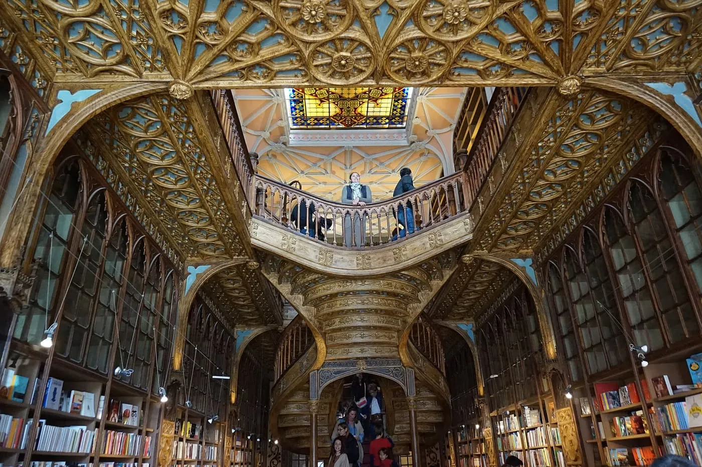 The double wooden staircase of Livraria Lello rising to a balcony under a stained-glass skylight, with bookcases on both sides