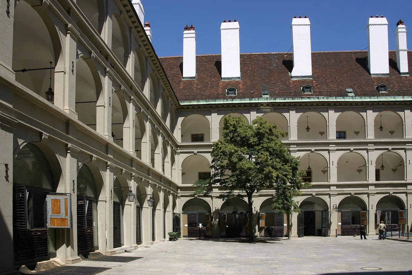 The arcaded courtyard of the Stallburg with a tree in the middle, white chimneys on the roof and arched stable doors on the ground floor