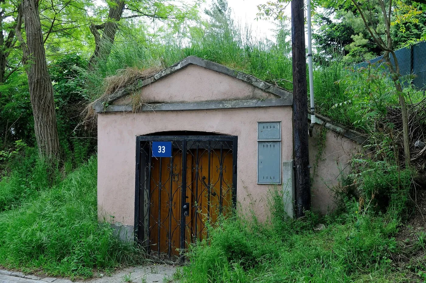 A low pink-rendered wine cellar with a pedimented front and a wrought-iron gate, number 33, set into a grassy bank