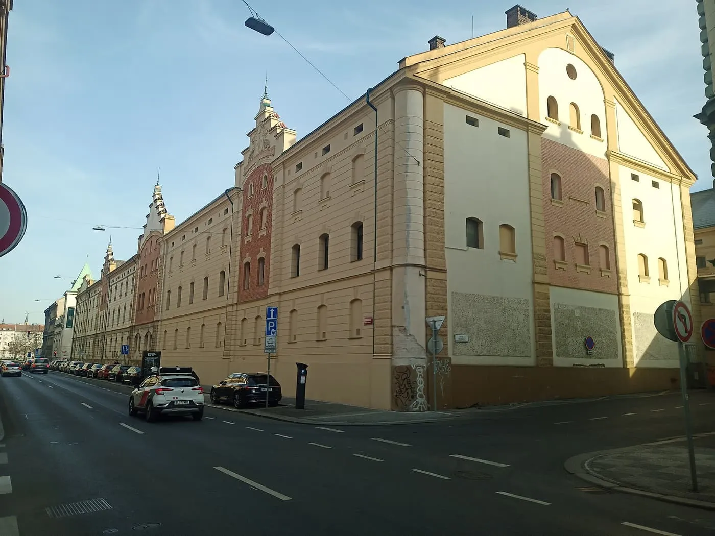 A long street front of the Staropramen brewery buildings in Smíchov, with gabled red-brick and cream-rendered sections, seen from the corner of Vltavská