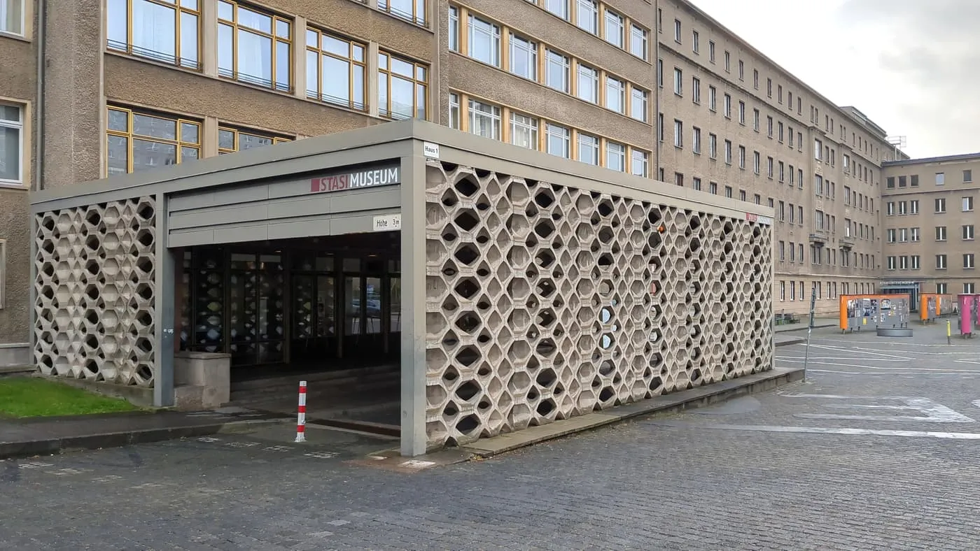 The concrete lattice canopy over the entrance to the Stasi Museum, with the long brick-and-render wing of Haus 1 rising behind it