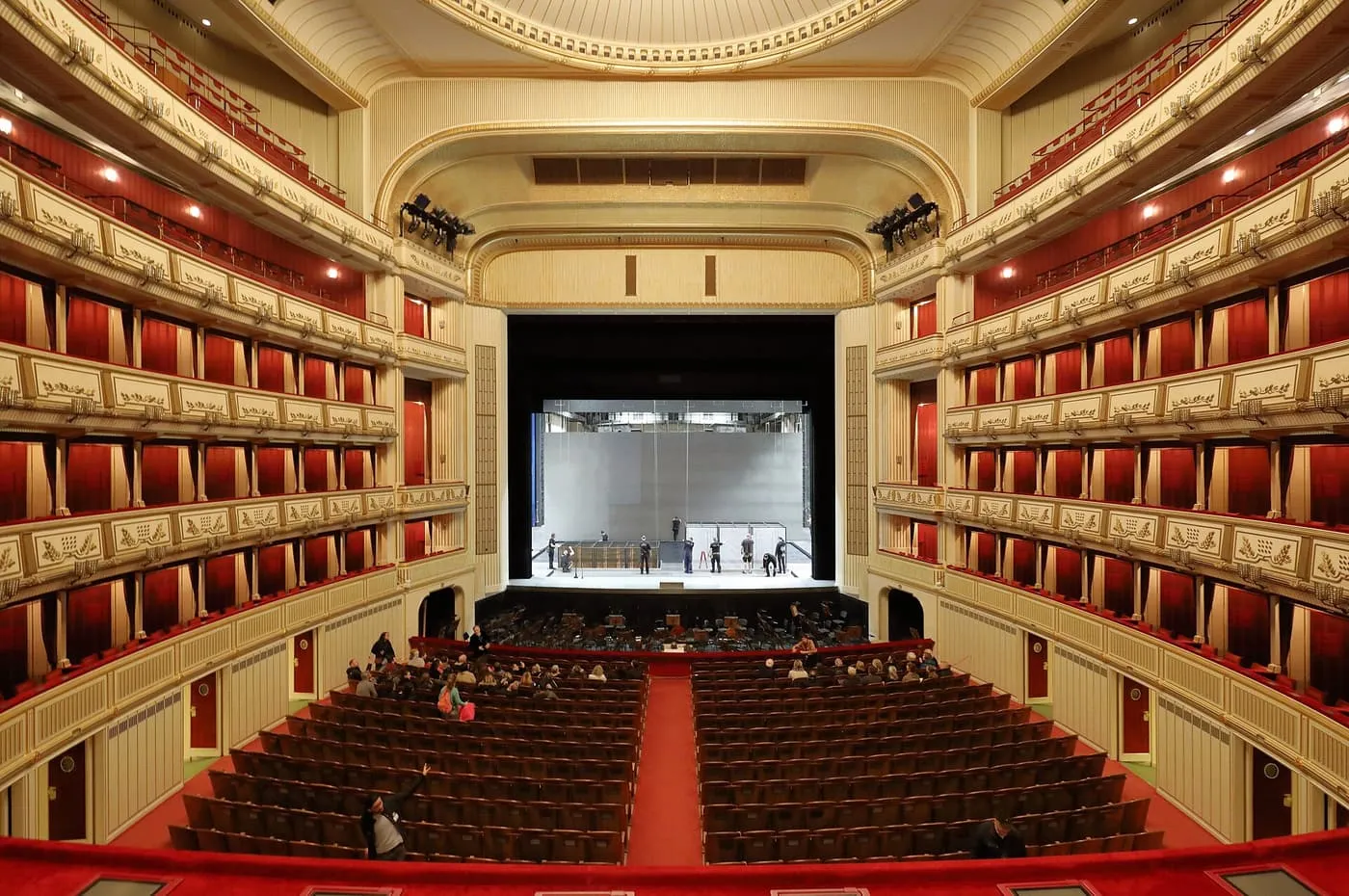 The auditorium of the Vienna State Opera seen from the back of the stalls, with tiers of boxes hung in red and the stage ahead