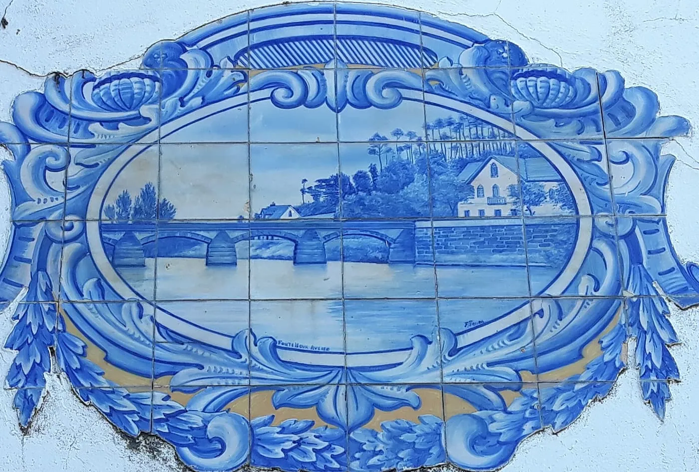 A blue and white tile panel of a bridge and a house across the water, in a scrolling frame, on a wall at Aveiro railway station