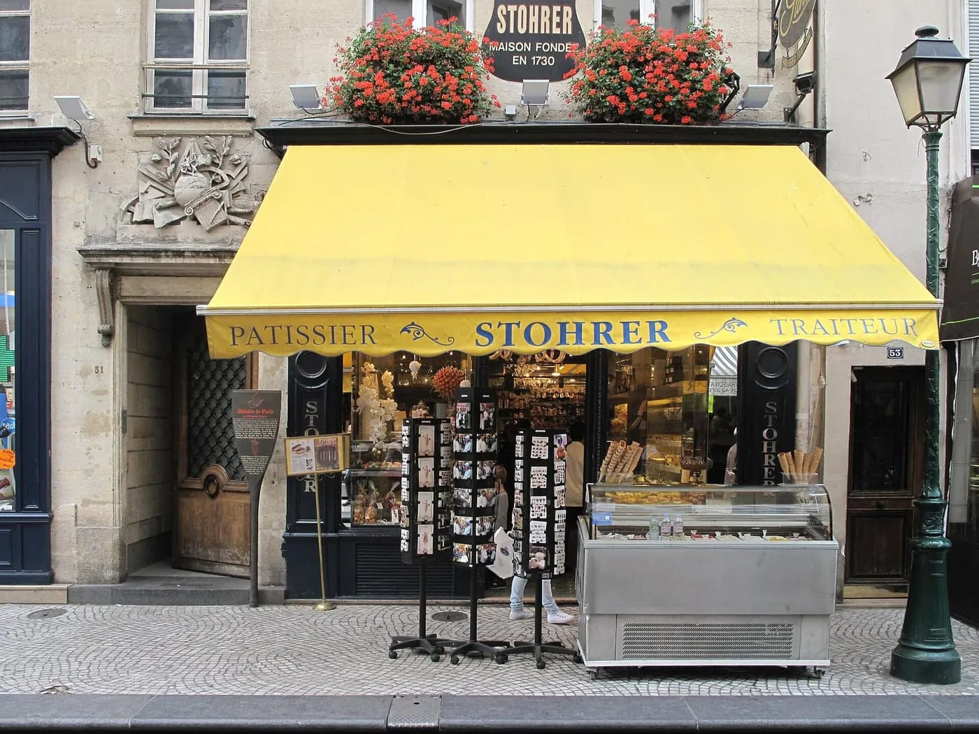 The shopfront of Stohrer on rue Montorgueil, with a yellow awning, red geraniums and a sign reading Maison fondée en 1730