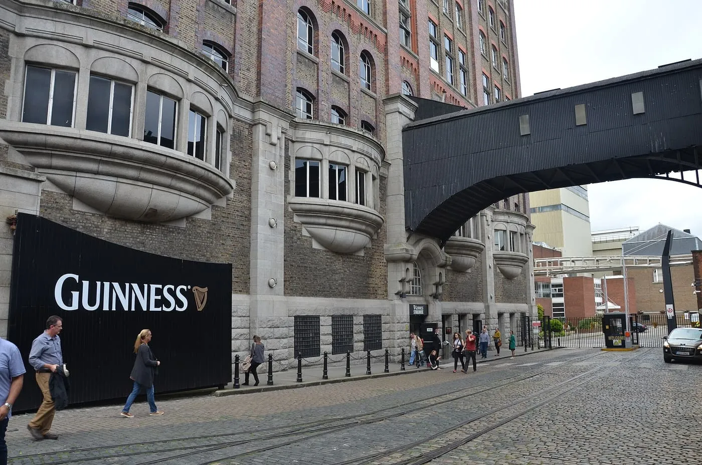 The brick and stone front of the Guinness Storehouse with curved bay windows, a black Guinness gate and a covered walkway across the street