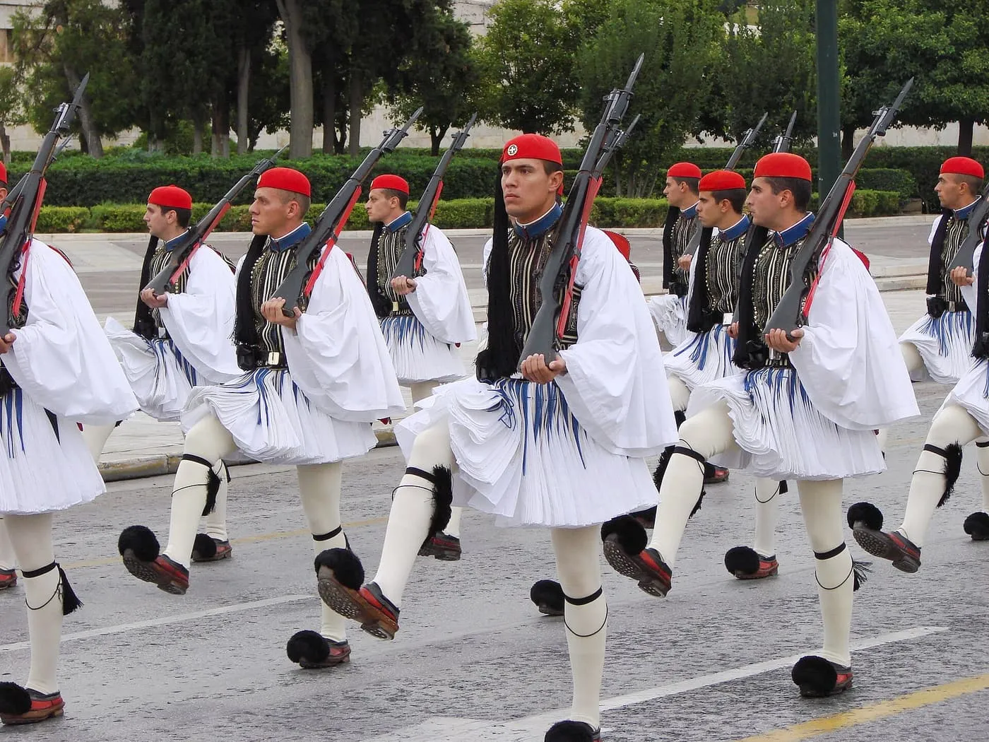 A column of Evzones marching in white fustanella kilts, red caps and tasselled shoes, rifles on their shoulders