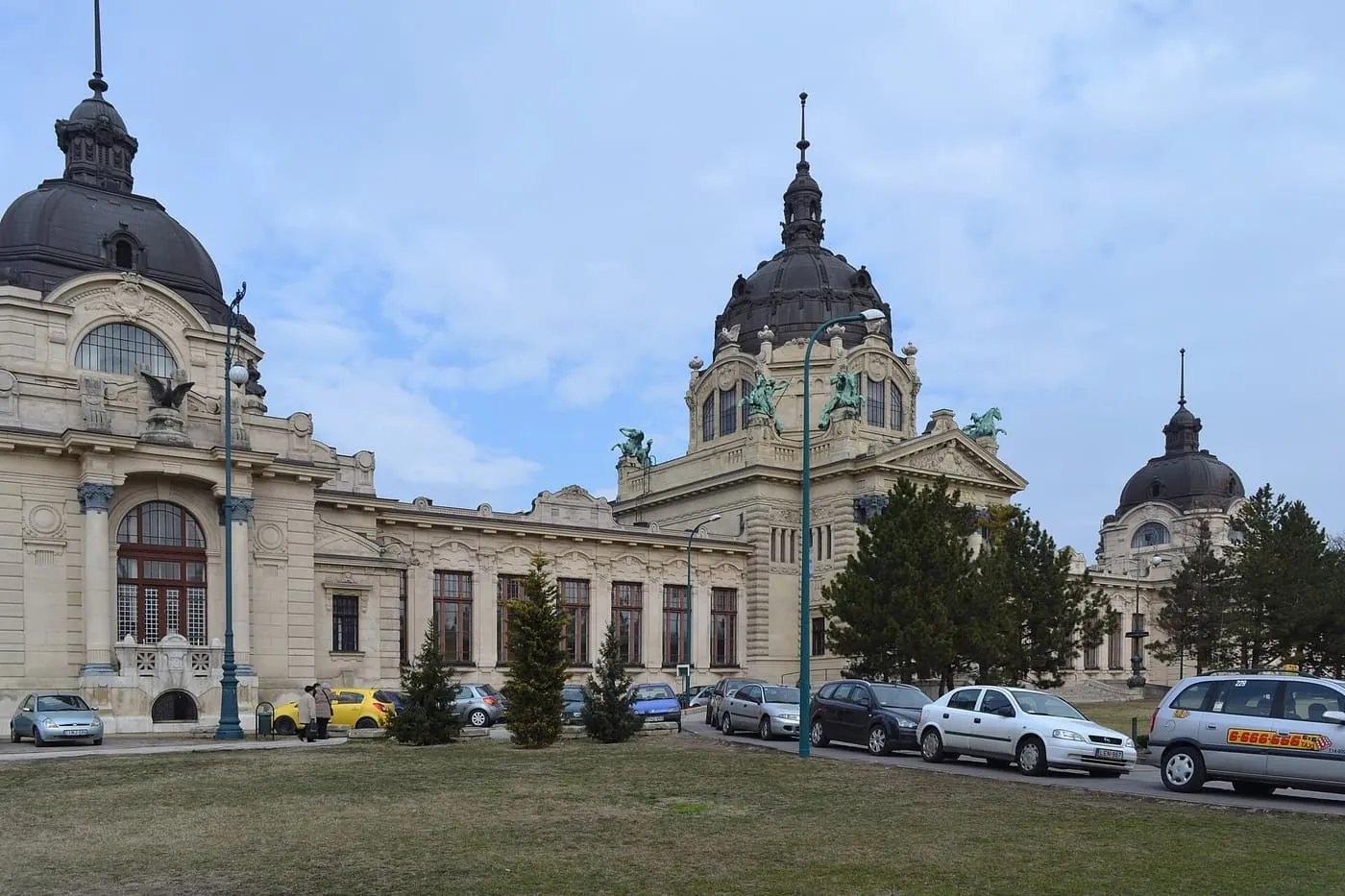 The domed Neo-baroque street front of the Széchenyi Baths in the City Park, with parked cars along the road