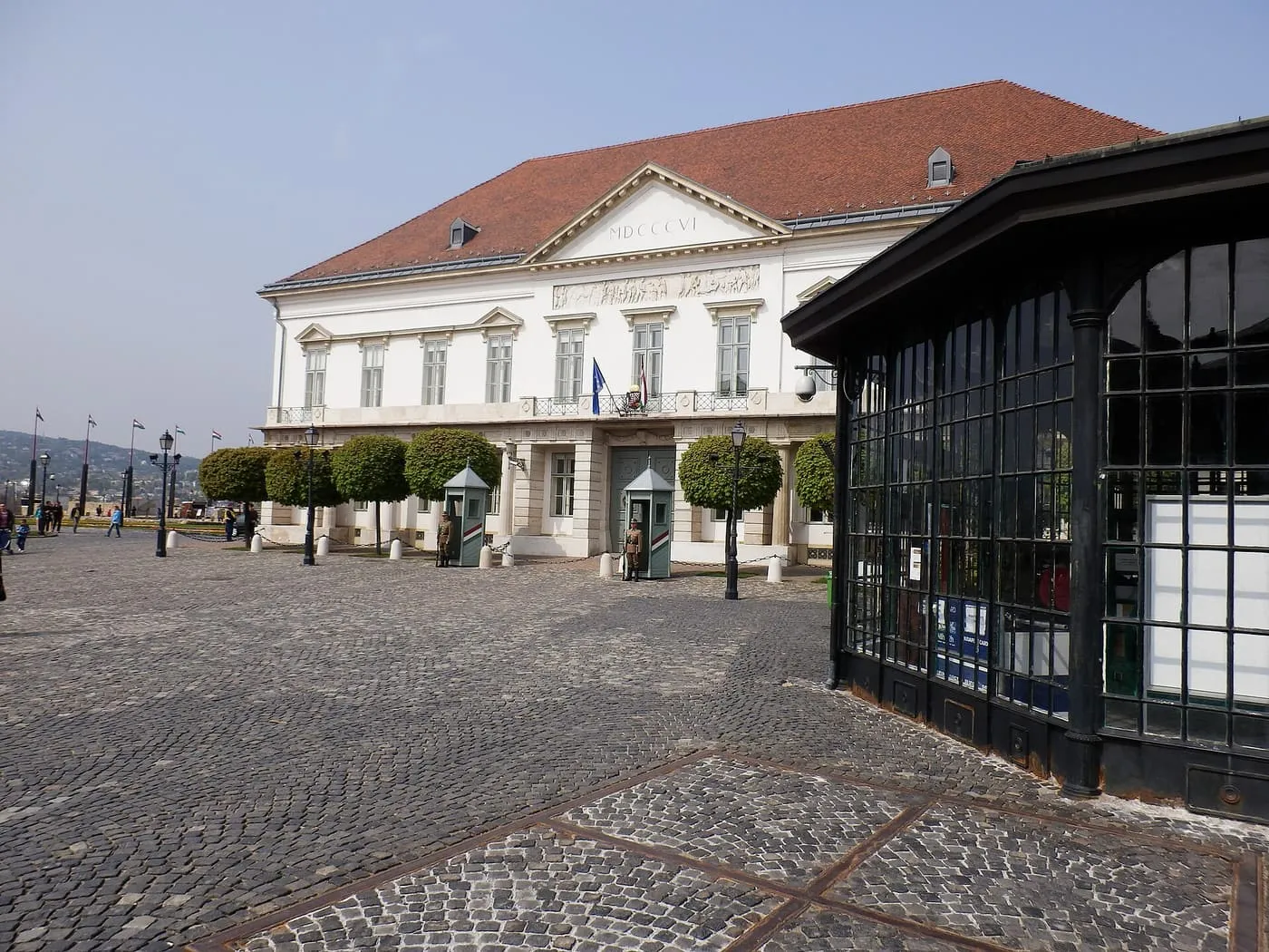 The white Sándor Palace beside the glass pavilion of the funicular's upper station on the cobbled Szent György tér