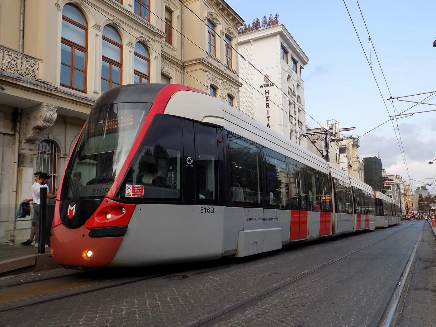 A red and grey T1 tram standing at a stop on a cobbled street in Sultanahmet, with historic buildings and overhead wires above it