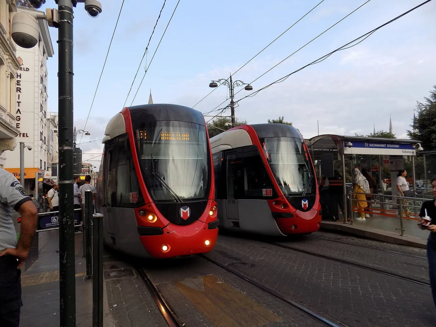 Two red T1 trams at the Sultanahmet stop, with passengers on the platform beside them