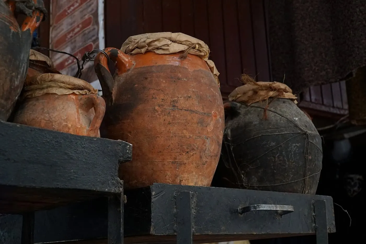 Terracotta tanjia jars with paper-covered tops on a dark shelf in a Marrakech souk