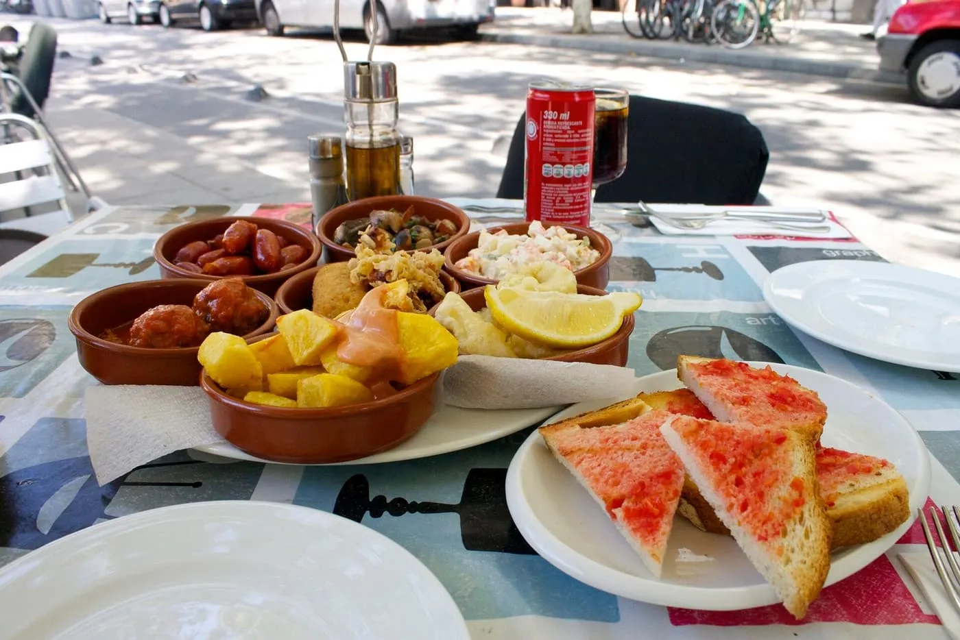 A pavement table with small terracotta dishes of tapas with lemon and pineapple, and a plate of toasted bread rubbed with tomato