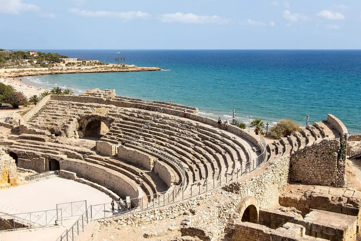 The curved stone tiers of Tarragona's Roman amphitheatre above a sandy beach and the blue Mediterranean
