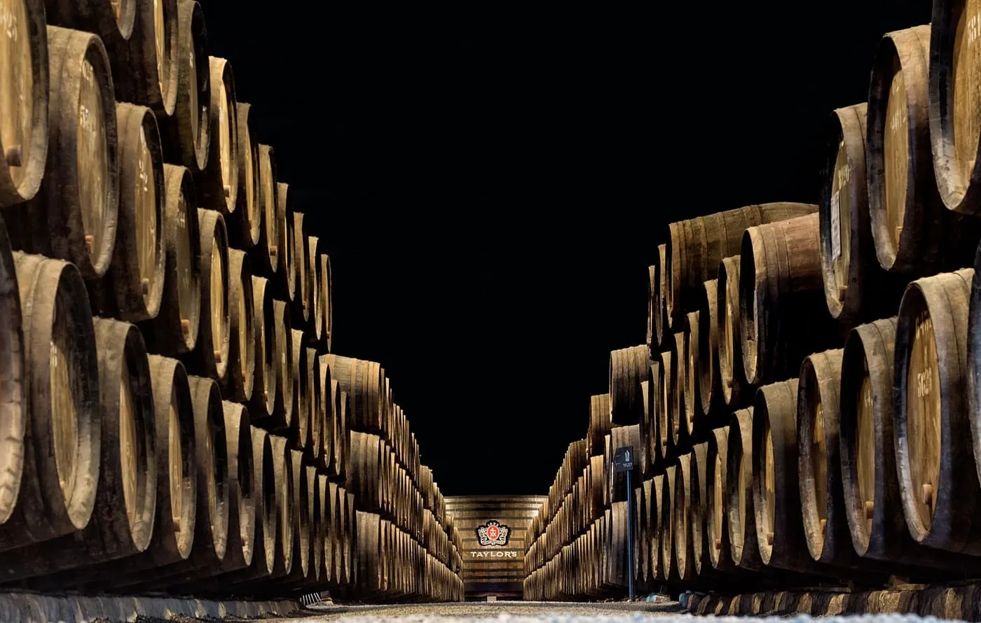 Two tall stacks of old port casks lining a dark cellar, with the Taylor's crest on the far wall