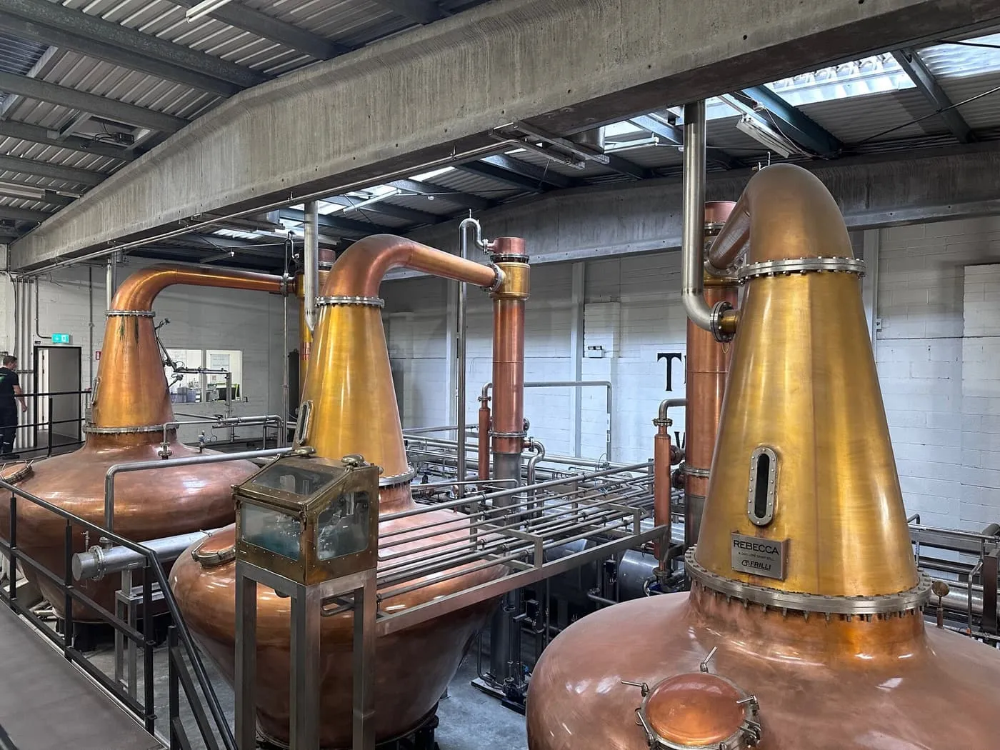 Three copper pot stills standing in a bright distillery hall at Teeling