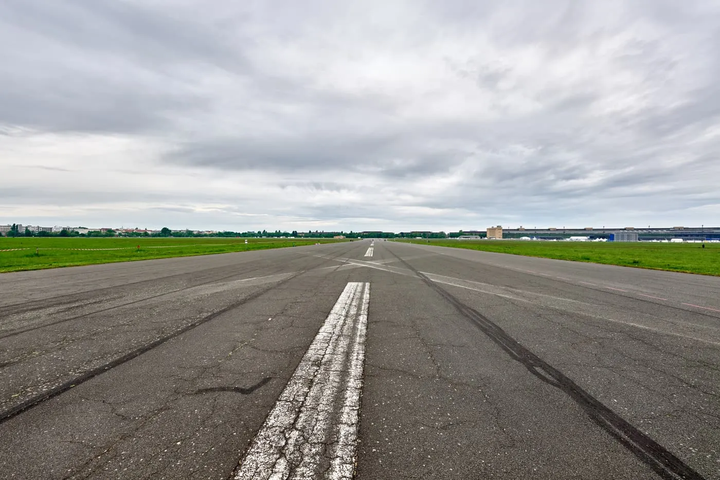 A runway of the former Tempelhof airport, with a worn white centre line leading across open grass towards the terminal building on the horizon