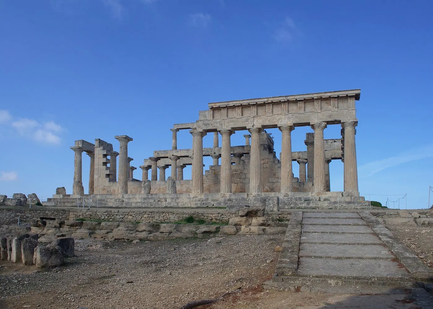 The Doric columns of the Temple of Aphaia on Aegina under a blue sky, with a stone ramp leading up to it