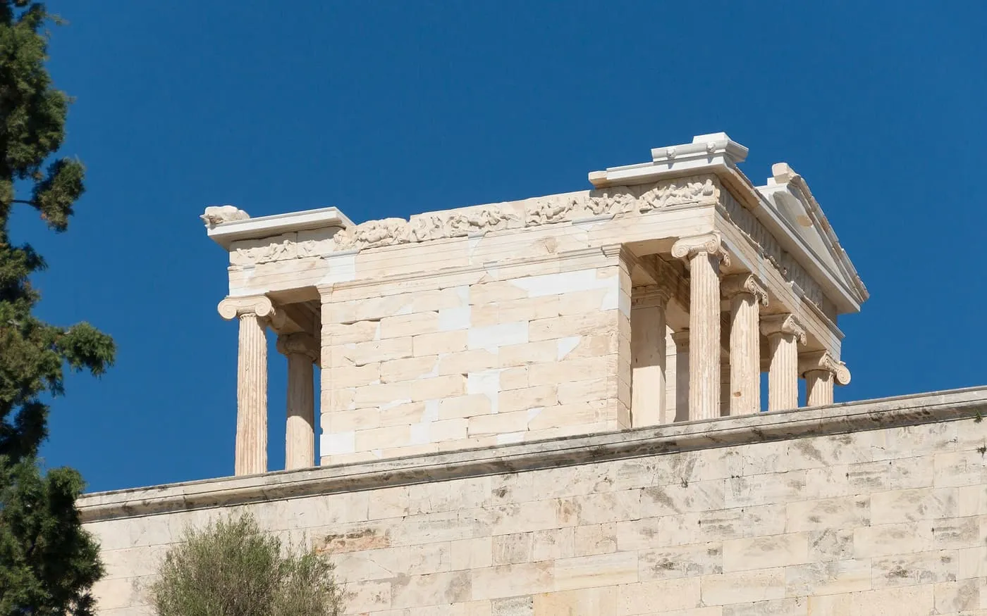 The small Ionic Temple of Athena Nike on its bastion, seen from below against a deep blue sky, with slender fluted columns and a carved frieze