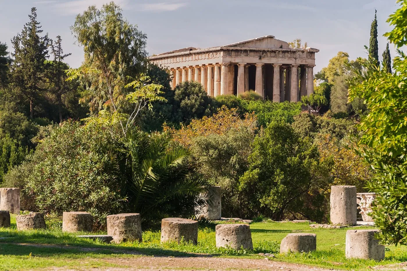The Temple of Hephaestus on its hill above trees, with the stone column drums of the Agora in the grass in front