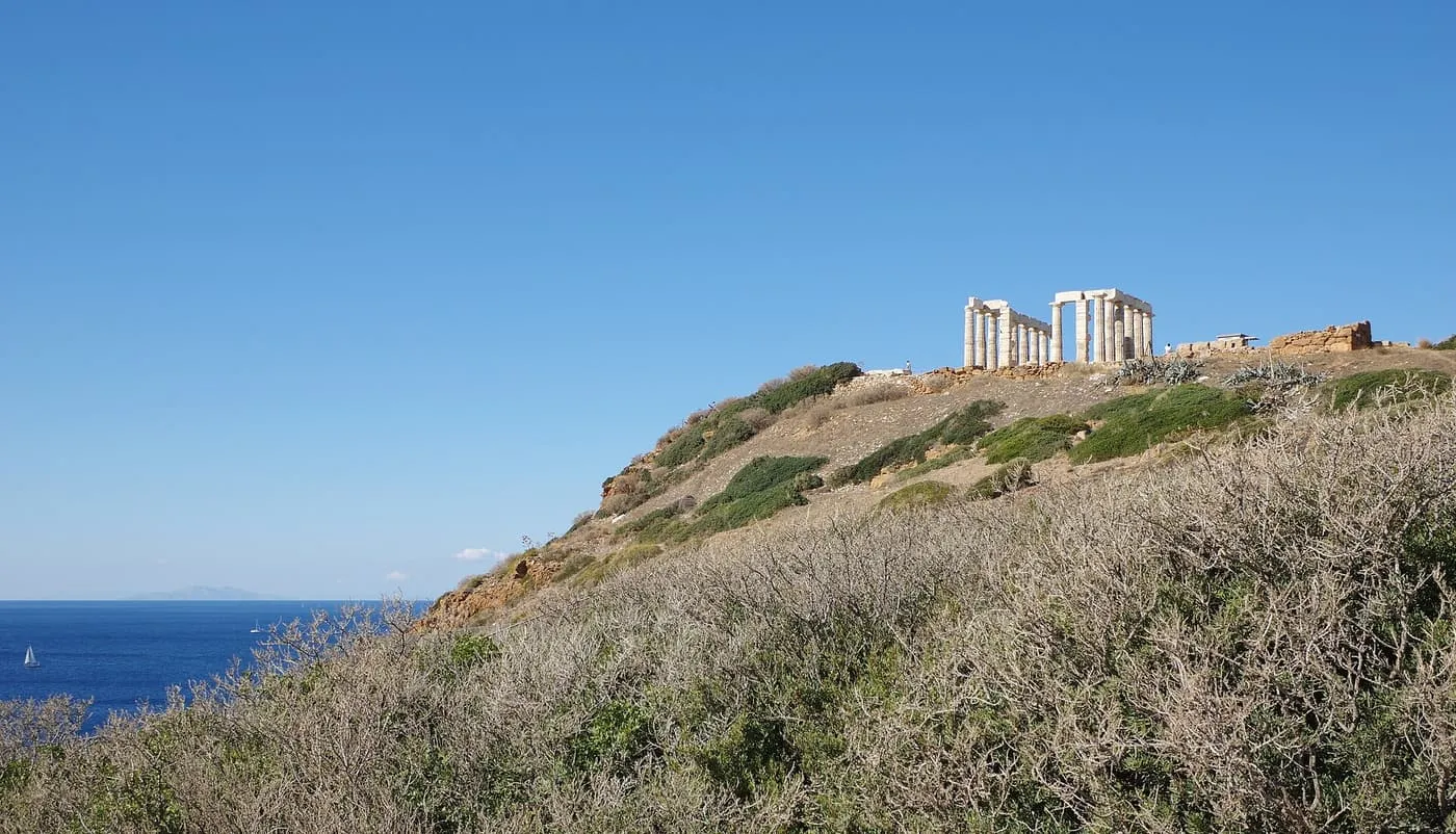The white columns of the Temple of Poseidon on top of its headland, with the sea and a sailing boat to the left