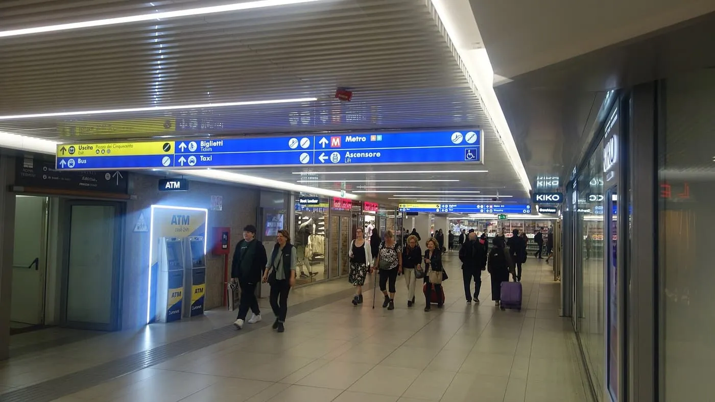 The lower concourse at Roma Termini, with blue signs for the metro, taxis and tickets above shopfronts
