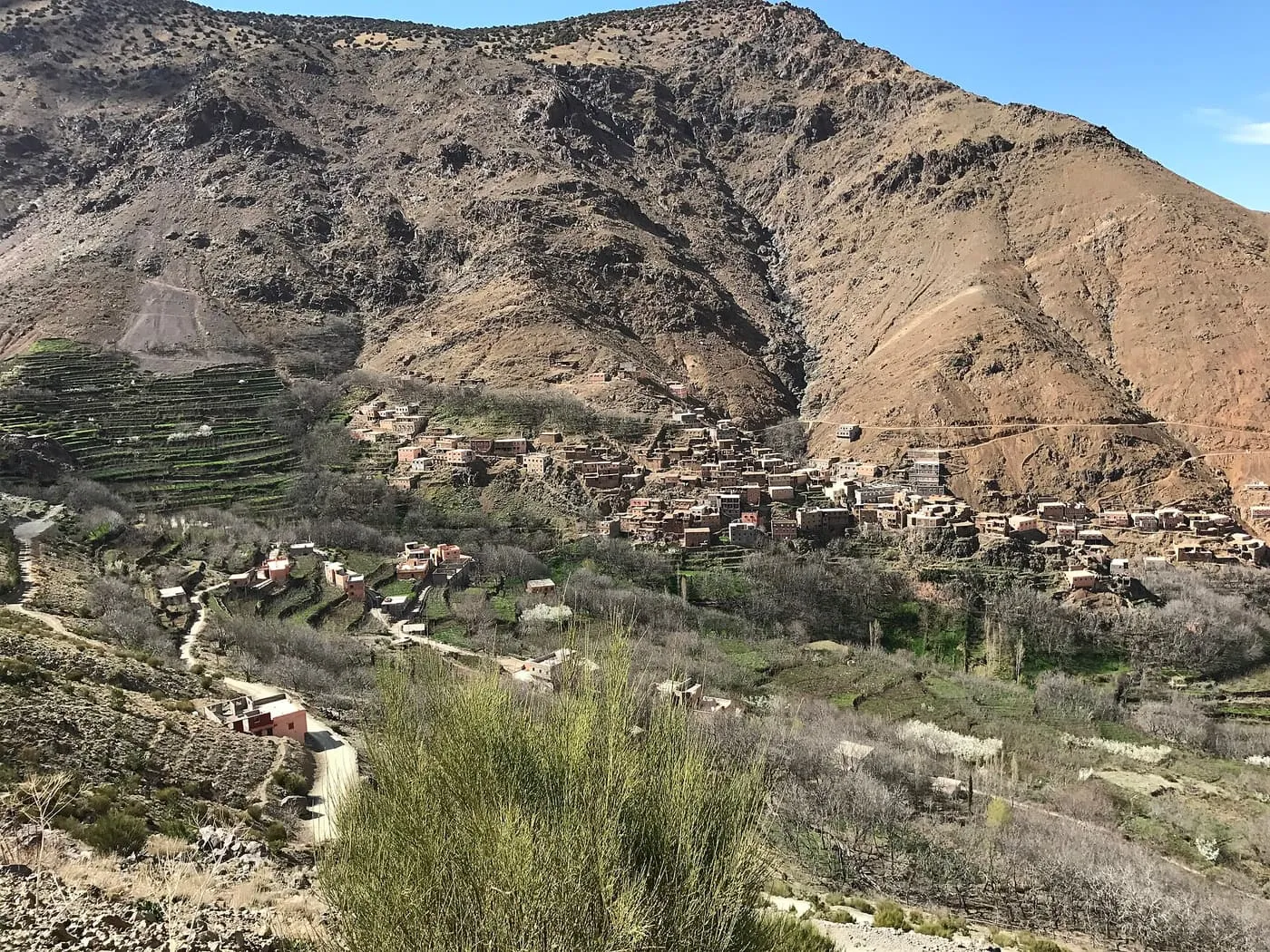 A stone-built village and green terraced fields on a steep brown mountainside above Imlil