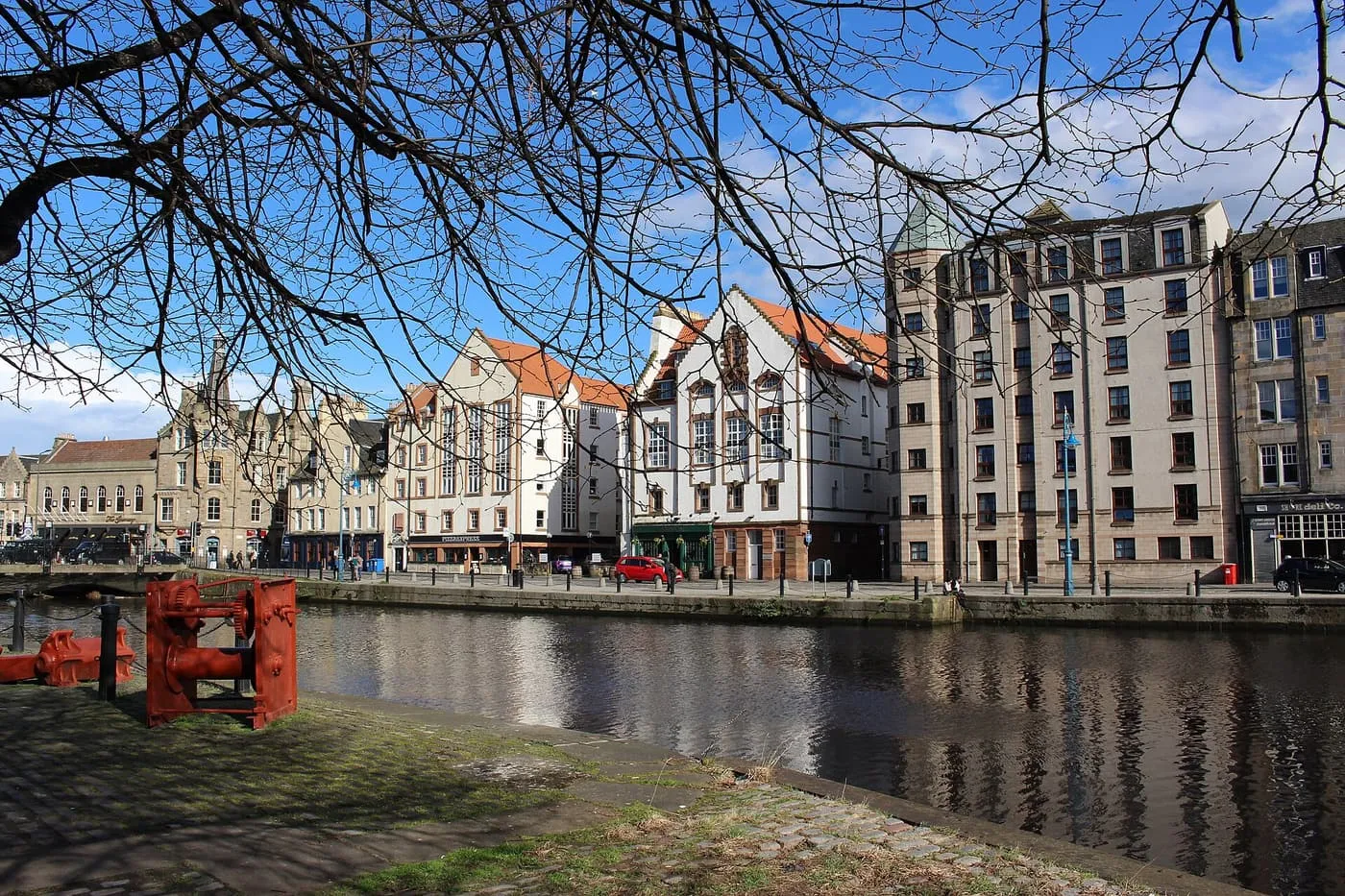 Tall pale tenements and gabled buildings along the quayside at the Shore in Leith, across the water and through bare branches
