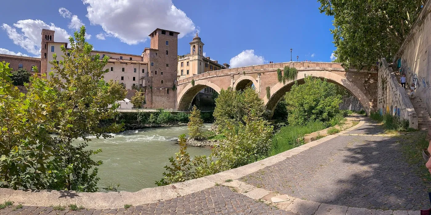 Ponte Fabricio, a Roman bridge of three brick and stone arches, crossing a green stretch of the Tiber to Tiber Island, with a medieval tower behind it